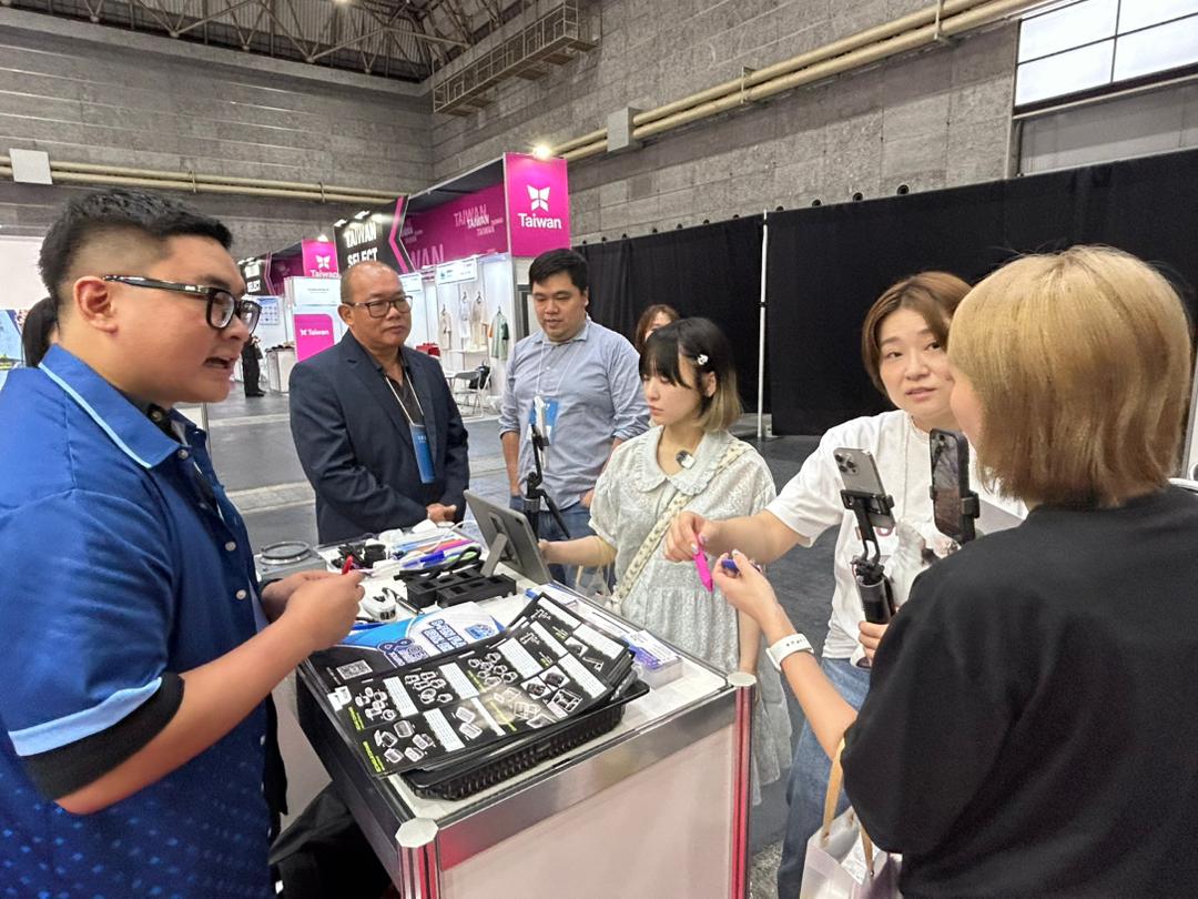 Team member demonstrating molded parts to visitors filming at the booth